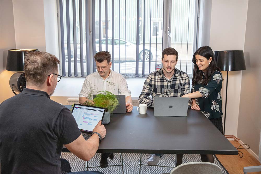 Ett grupp kollegor sitter i ett mötesrum och arbetar på sina datorer.